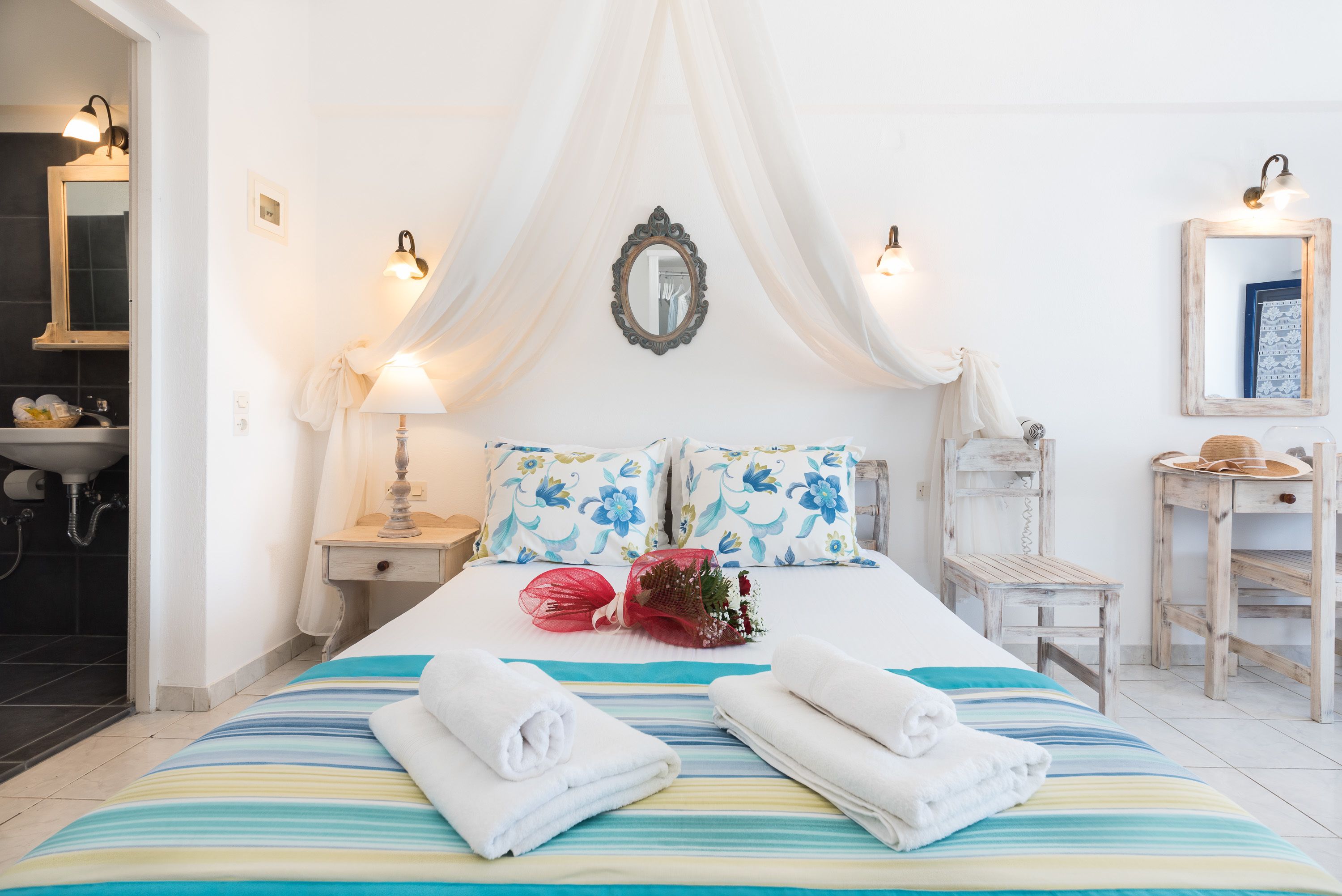 Ein Hotelzimmer mit Bett, Nachttisch, Schminktisch mit Spiegel und einem durchgegangenen Tür sichtbaren Badezimmer.