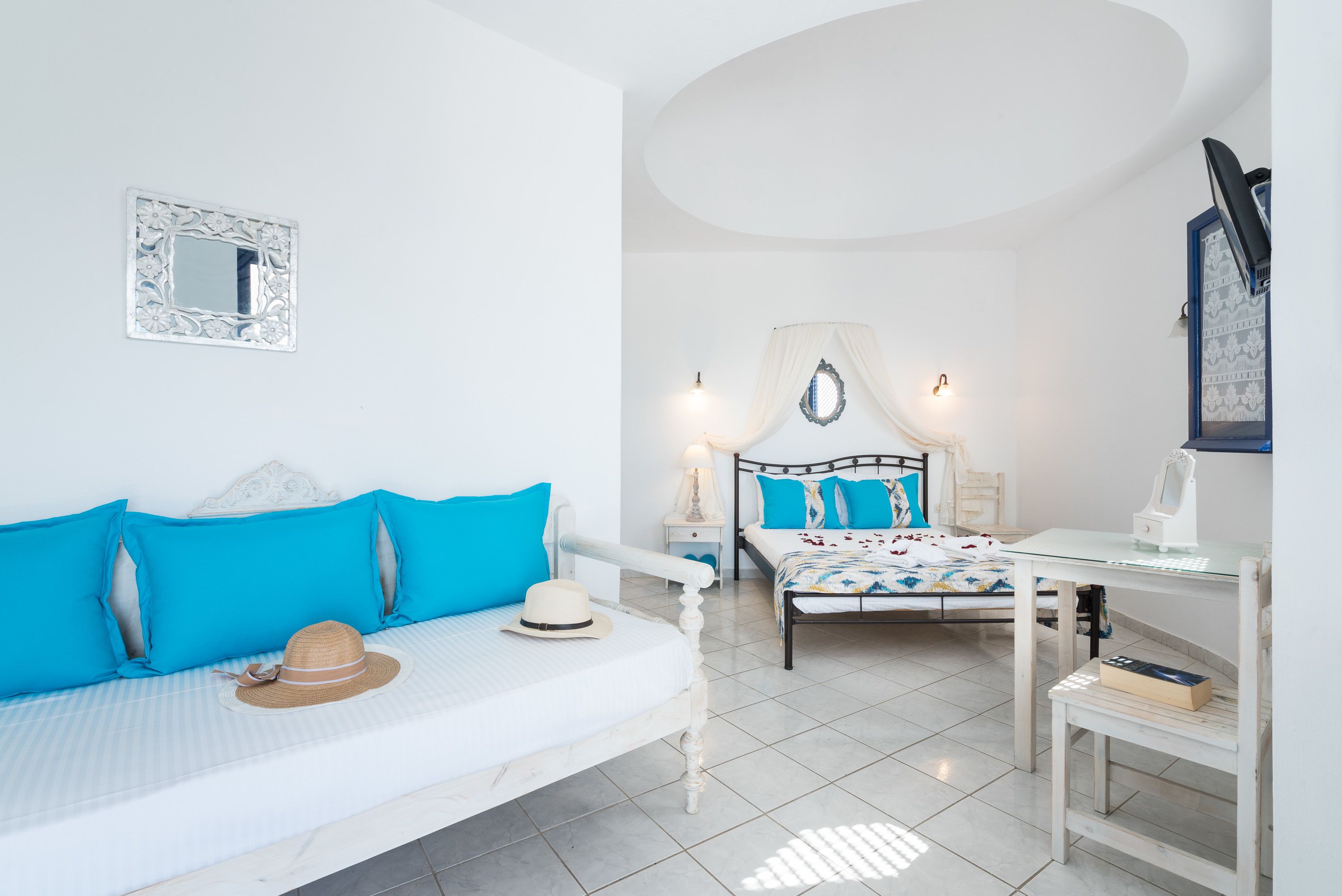A bedroom with a bed, a bedside table, a lamp, a mirror, and a window with a curtain.