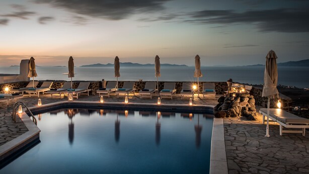 A serene poolside area with lounge chairs and umbrellas, a stone pool, and a view of the sea at sunset. - Agnadi View Villa (Santorini)