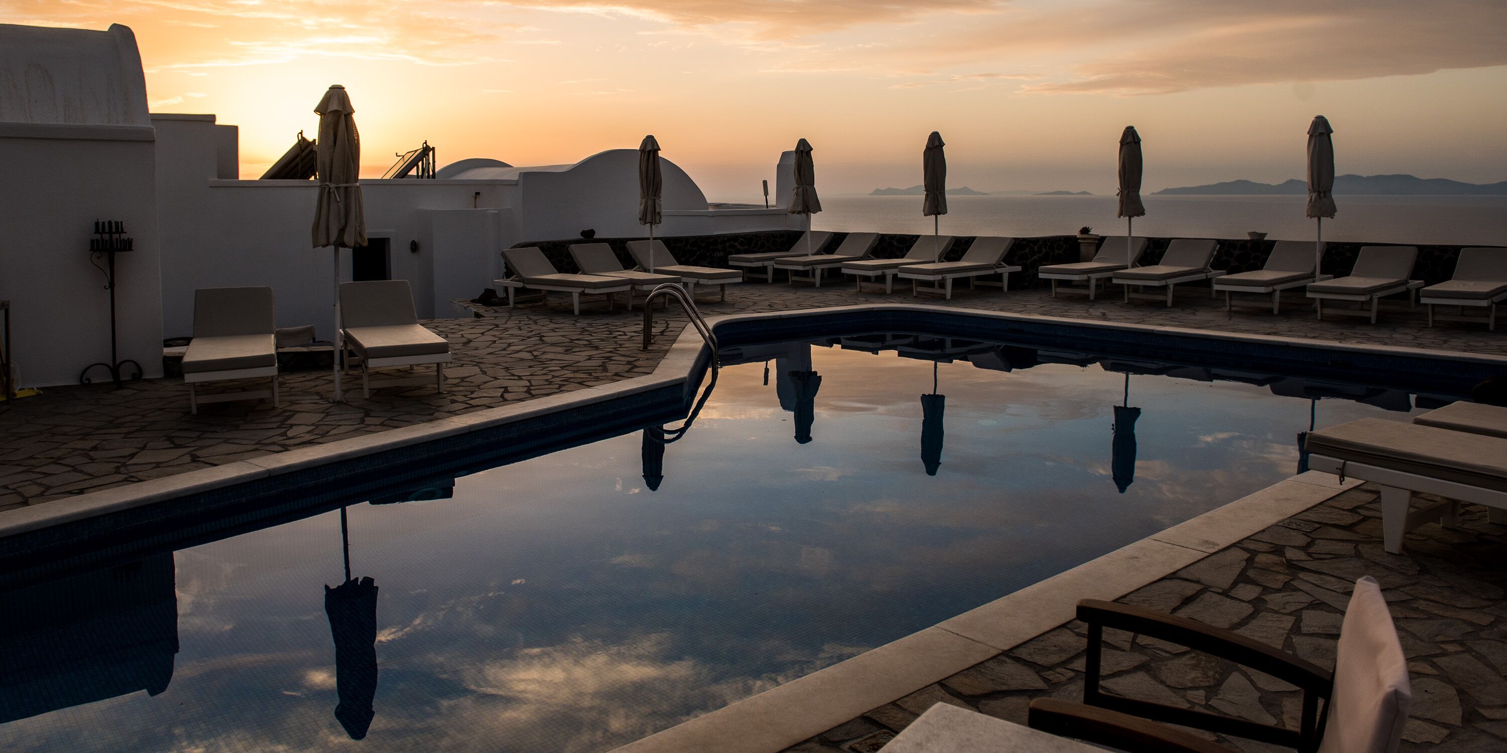 A rooftop pool with lounge chairs and umbrellas, reflecting the sunset.
