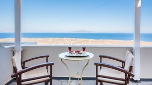 A balcony with two wooden chairs, a small round table with a white tray, and a view of the sea and beach. - Agnadi View Villa (Santorini)