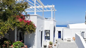 A white-walled building with a blue door, a pergola, and a view of the sea. - Agnadi View Villa (Santorini)