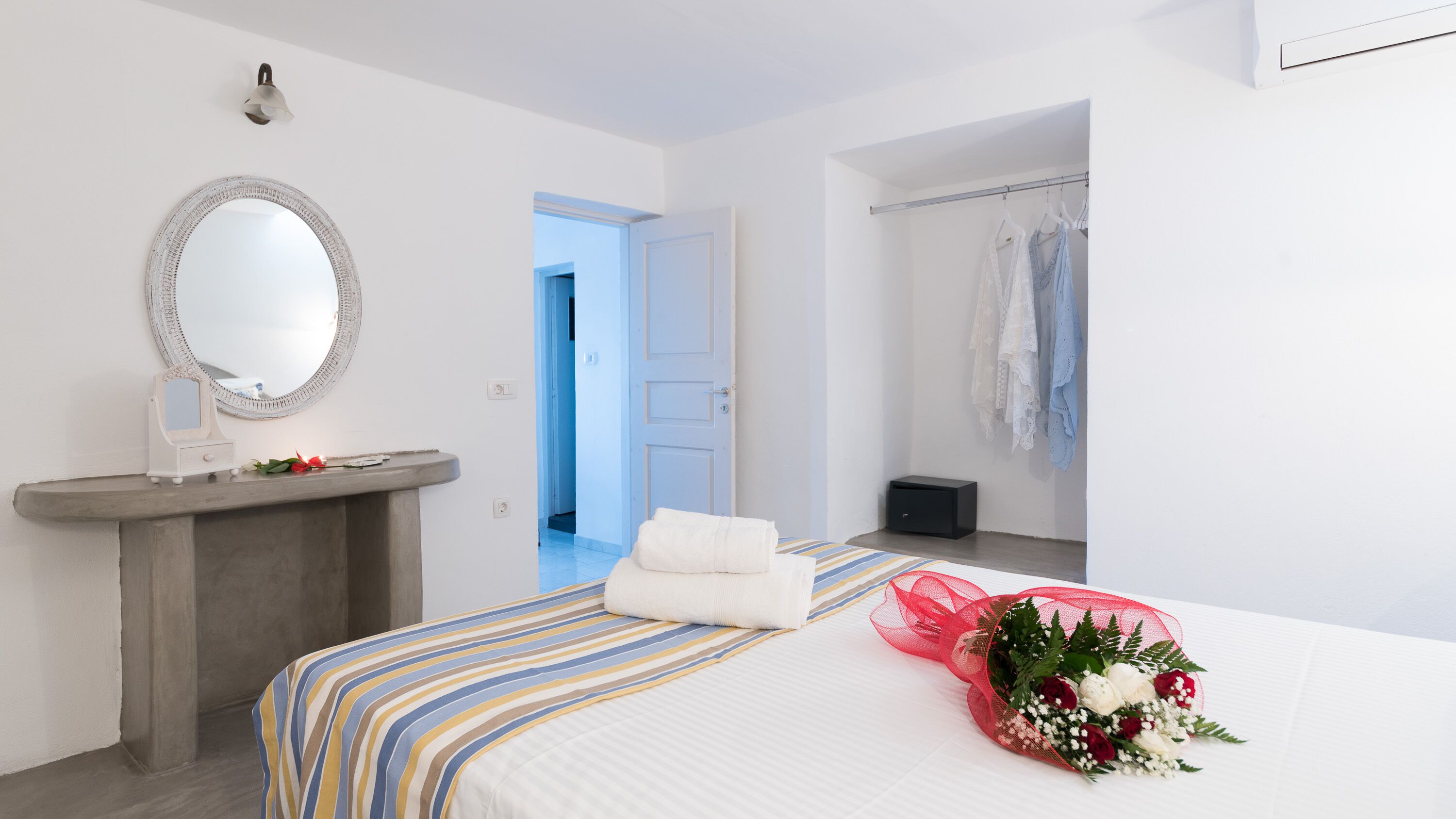 Ein Hotelzimmer mit Bett, Schminktisch mit Spiegel, kleinem Tisch, Bademantel und Blumenstrauß.
