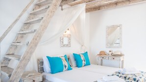 A bedroom with a wooden staircase, a bed with blue and white bedding, a bedside table, and a mirror on the wall. - Agnadi View Villa (Santorini)