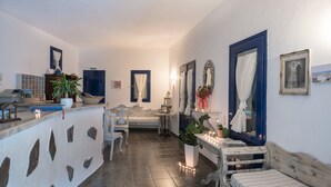 A hallway with a stone wall, a bed, a small table with candles, and a blue door. - Agnadi View Villa (Santorini)
