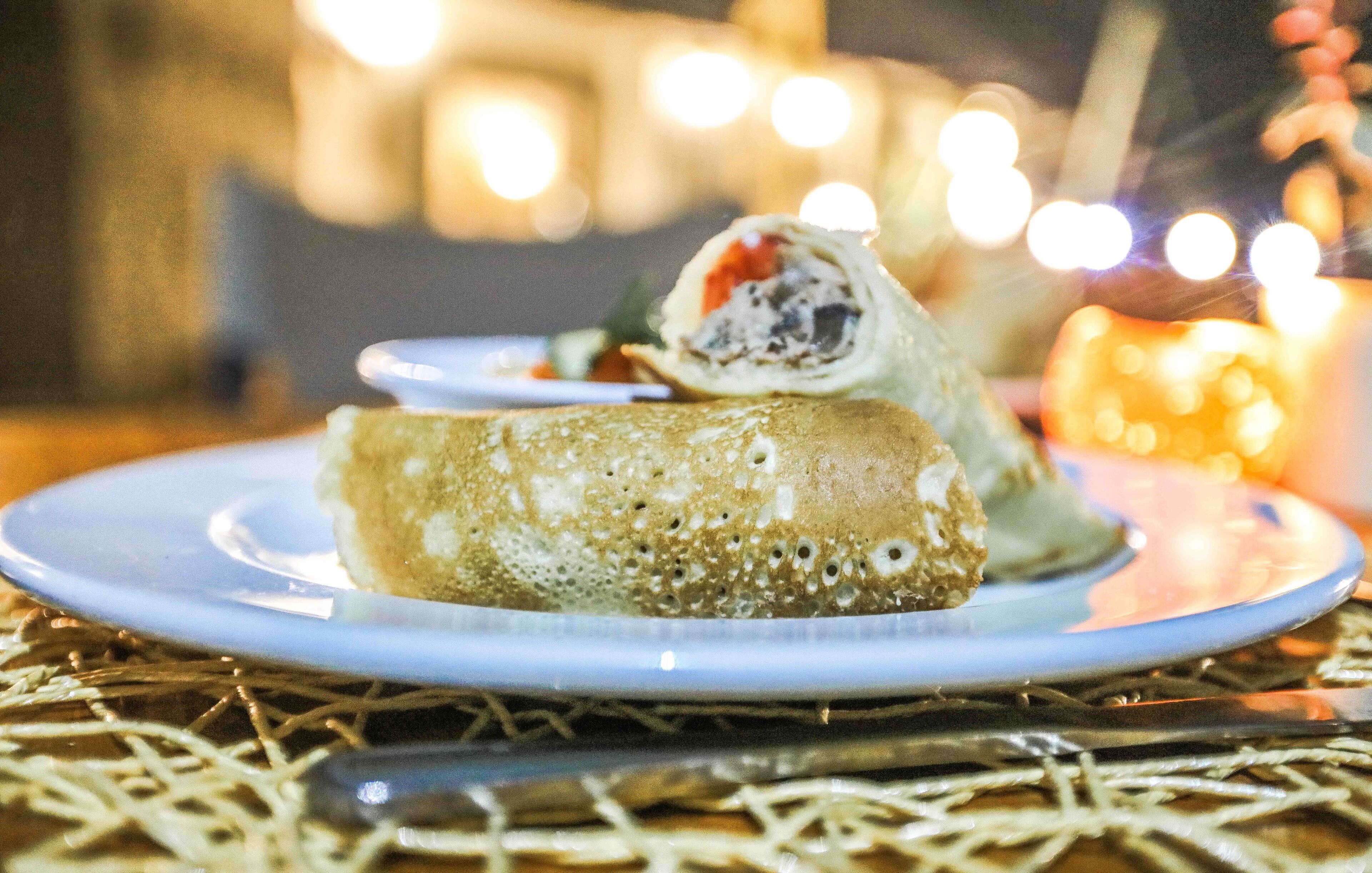 Un plato con un pastel enrollado sobre una mesa, con un tenedor y una vela al fondo.