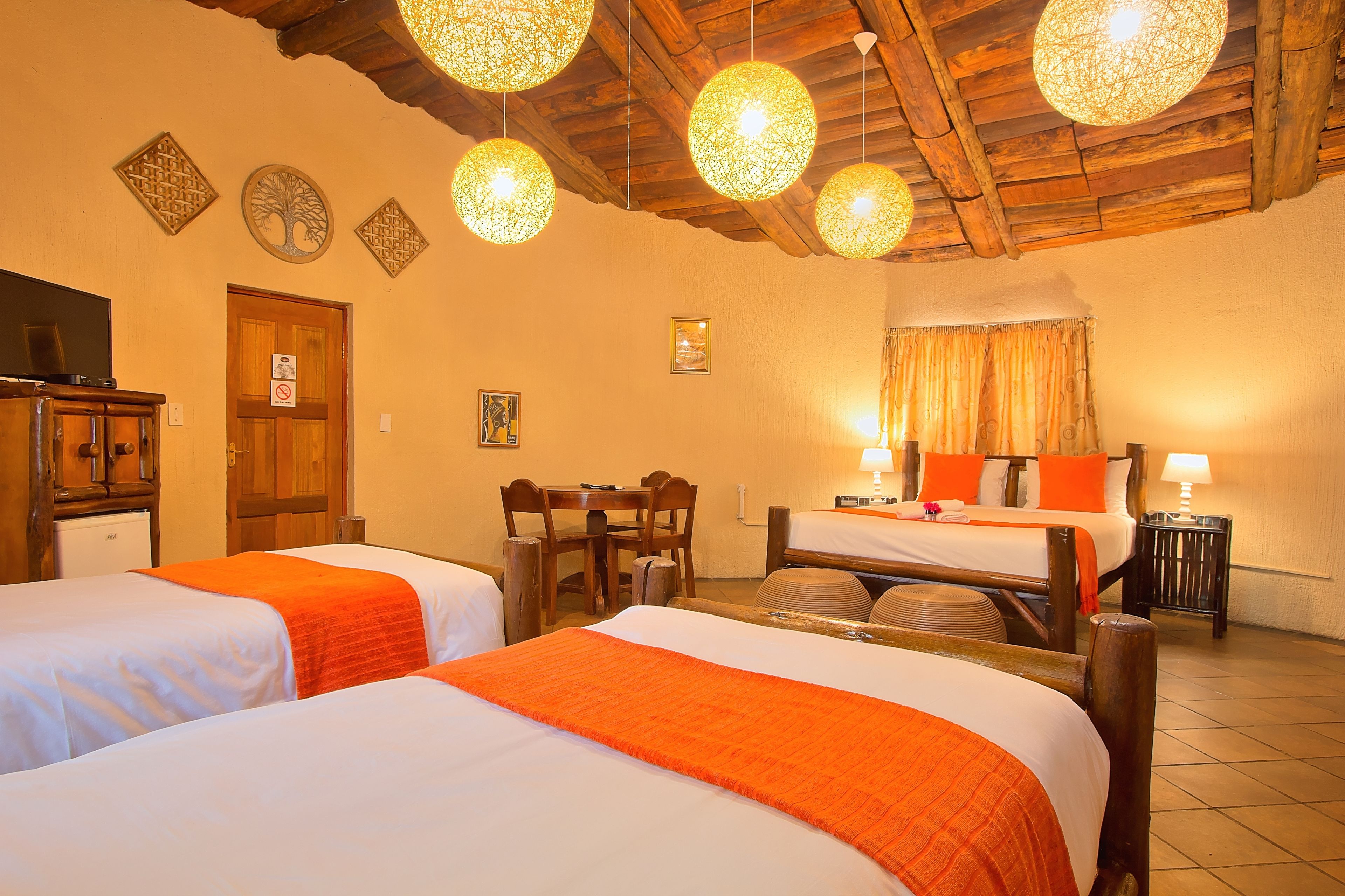 A hotel room with two beds, a wooden ceiling, and a dining area with a table and chairs.