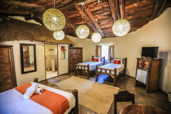 A rustic room with two wooden beds, a dining table, and a TV. - Kruger Adventure Lodge (Mbombela)