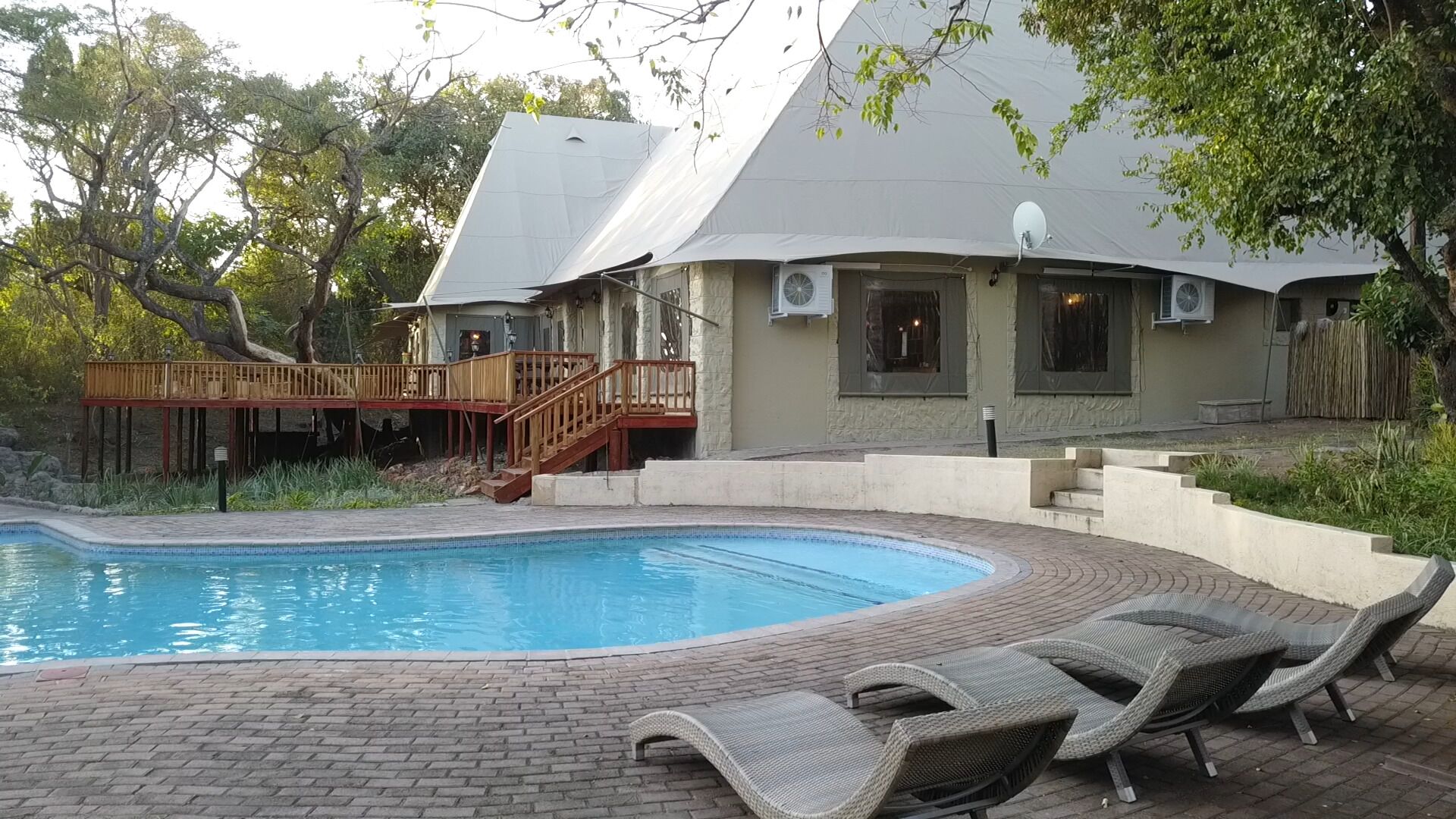 A swimming pool with a wooden deck and lounge chairs, surrounded by a house with a unique architectural design.