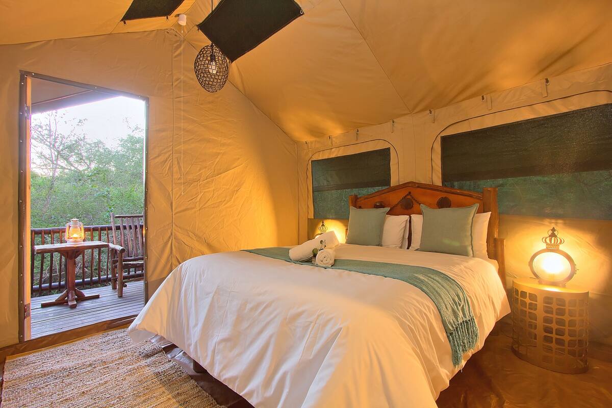 A tented room with a bed, bedside lamps, and a view of the outdoors.