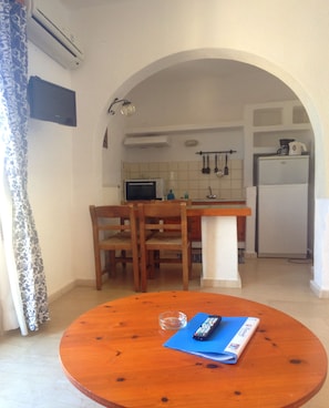 A small kitchen with a dining area, including a table with chairs, a microwave, and a refrigerator. - Mantraki Hotel Apartments (Agios Nikolaos)