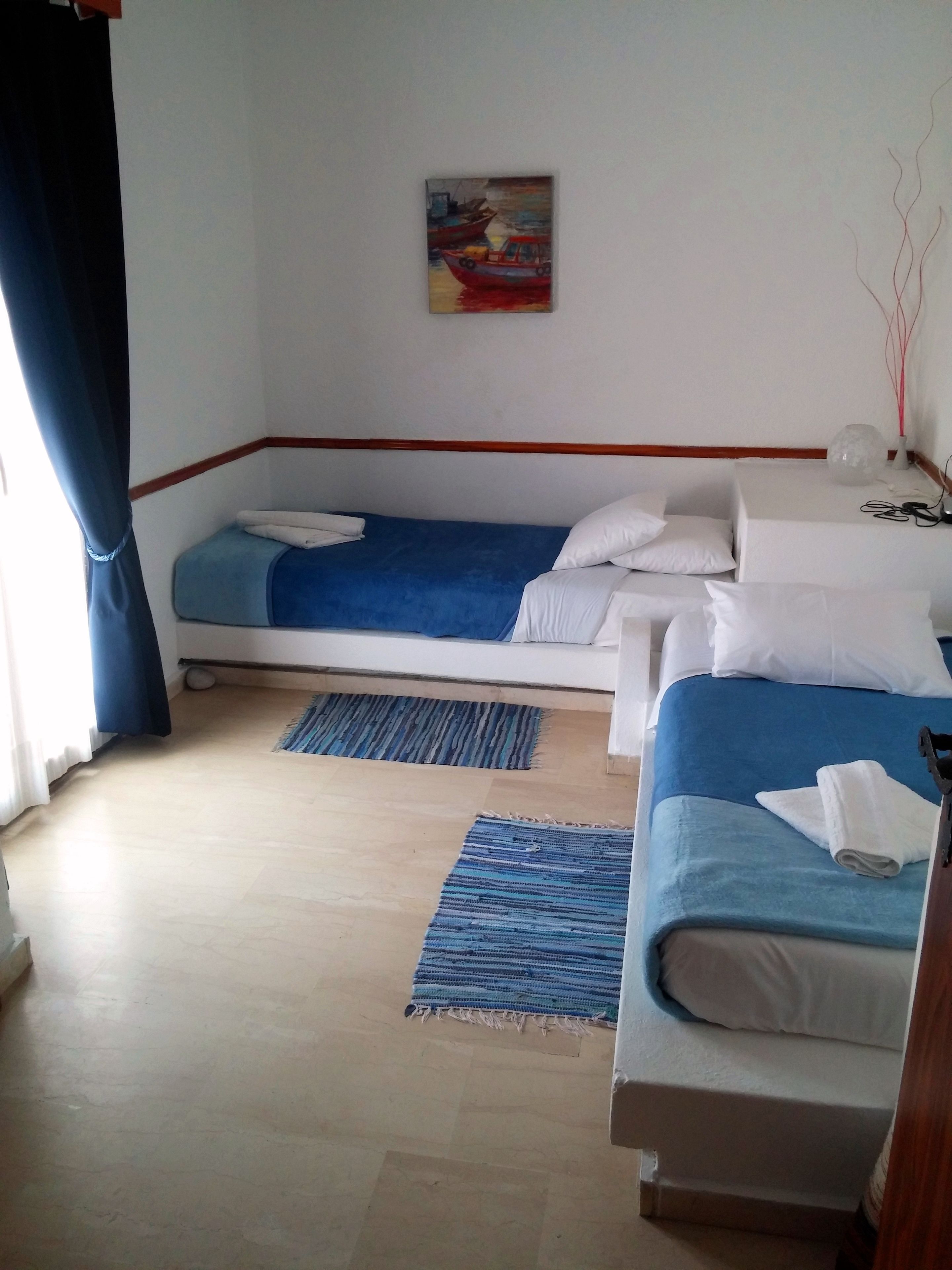 A hotel room with two beds, a painting on the wall, and a blue rug on the floor.