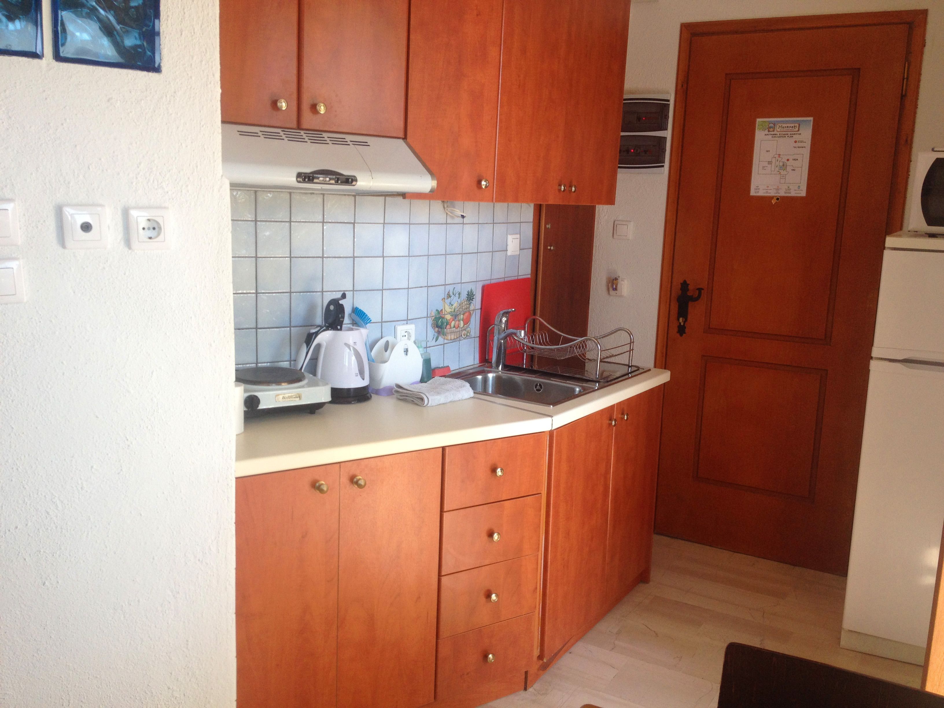Una cucina compatta con mobili in legno, un piano di lavoro bianco, un bollitore, un tostapane e un lavandino.