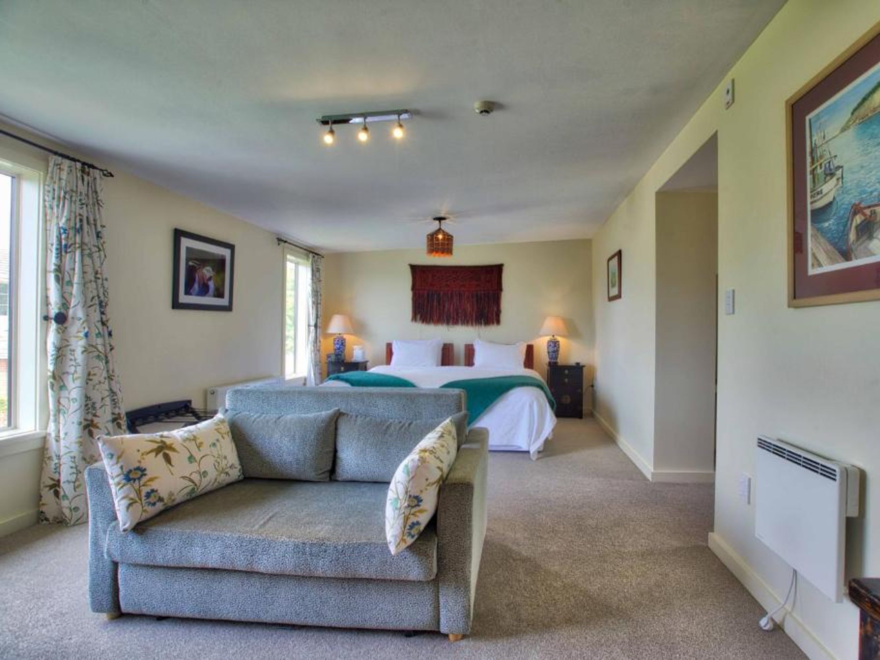 A bedroom with a bed, a sofa, two bedside tables with lamps, a radiator, and a window with curtains.