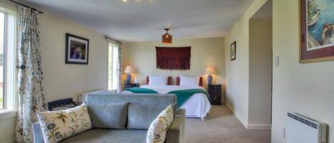 A bedroom with a bed, a sofa, two bedside tables with lamps, a radiator, and a window with curtains.