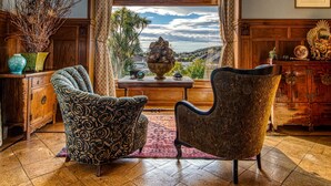 A room with a large window, two patterned armchairs, a wooden cabinet, and a vase with branches. - Pen-y-bryn Lodge (Oamaru)