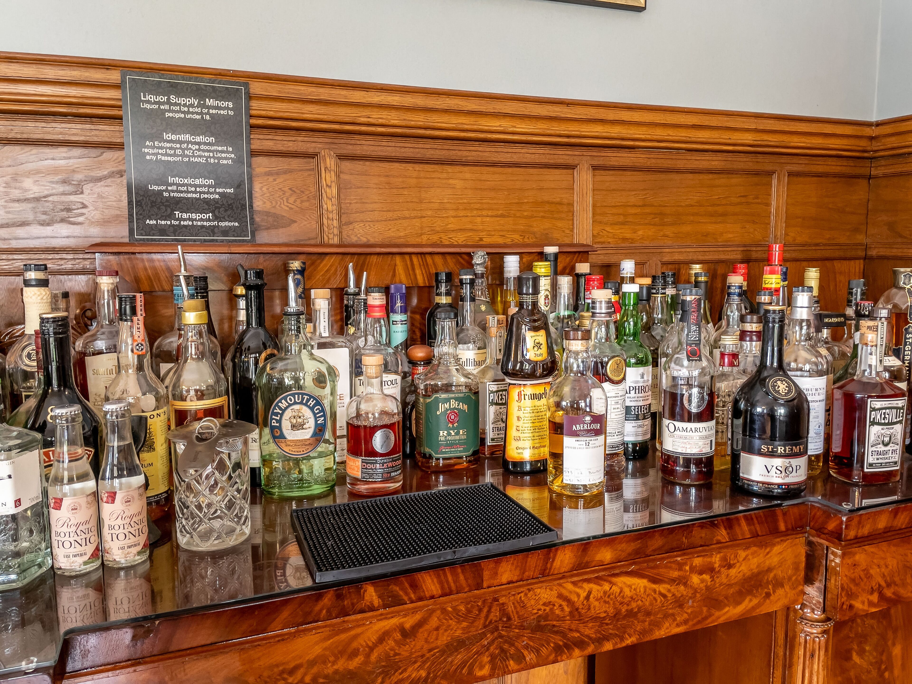 A bar counter with a variety of liquor bottles and a sign detailing liquor supply regulations.
