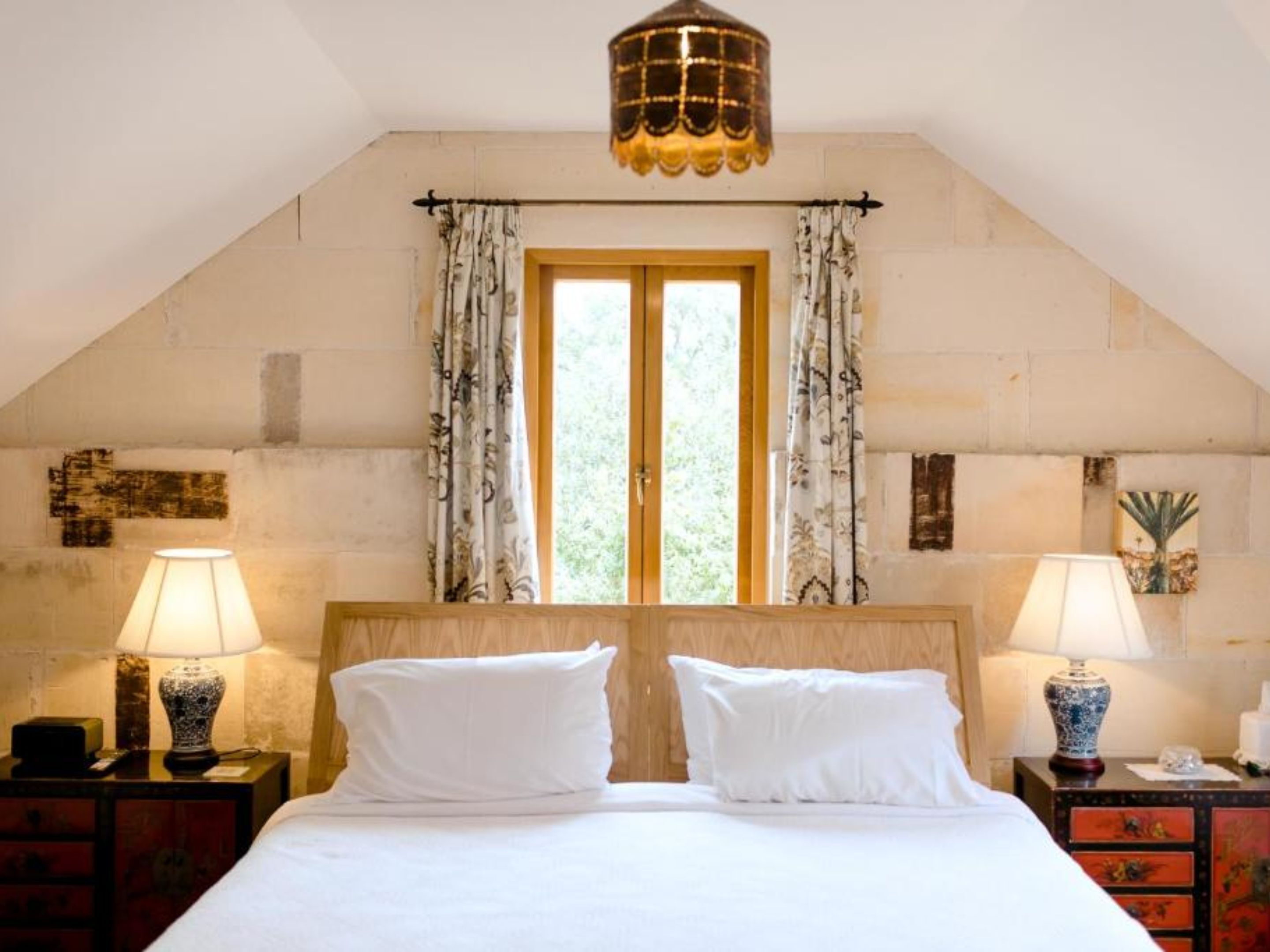 Une chambre à coucher avec un grand lit, deux tables de chevet avec des lampes, une fenêtre avec des rideaux et un luminaire décoratif au plafond.