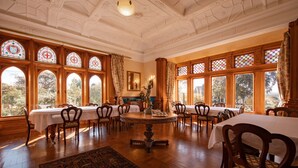 A dining room with a round table surrounded by chairs, large windows with stained glass, and a chandelier. - Pen-y-bryn Lodge (Oamaru)