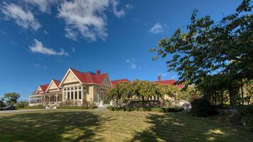 A large, elegant house with a red roof and multiple chimneys, surrounded by well-maintained lawns and trees.