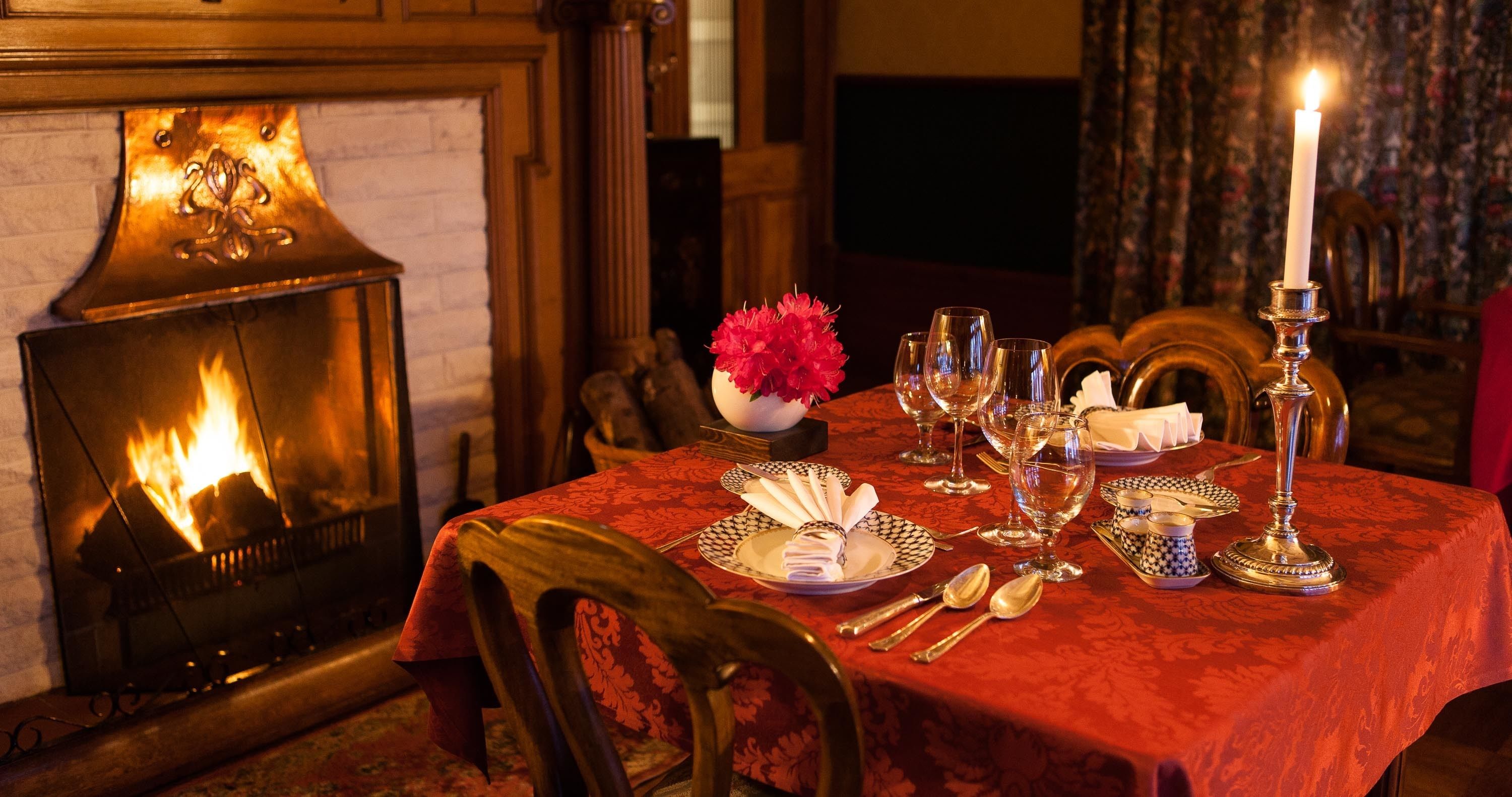 A dining table set with plates, cutlery, and glasses, a lit candle, and a fireplace with a fire.