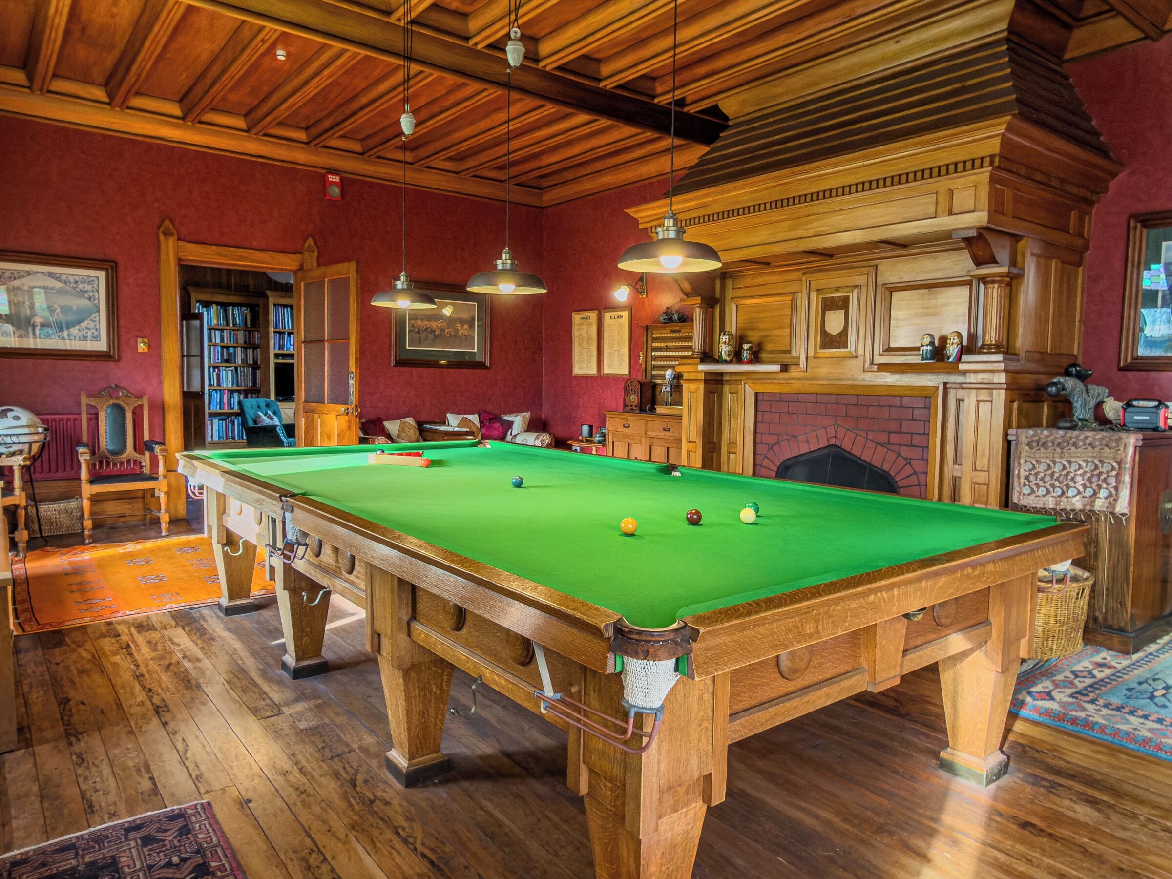 A pool table with balls, a bookshelf, and a fireplace.
