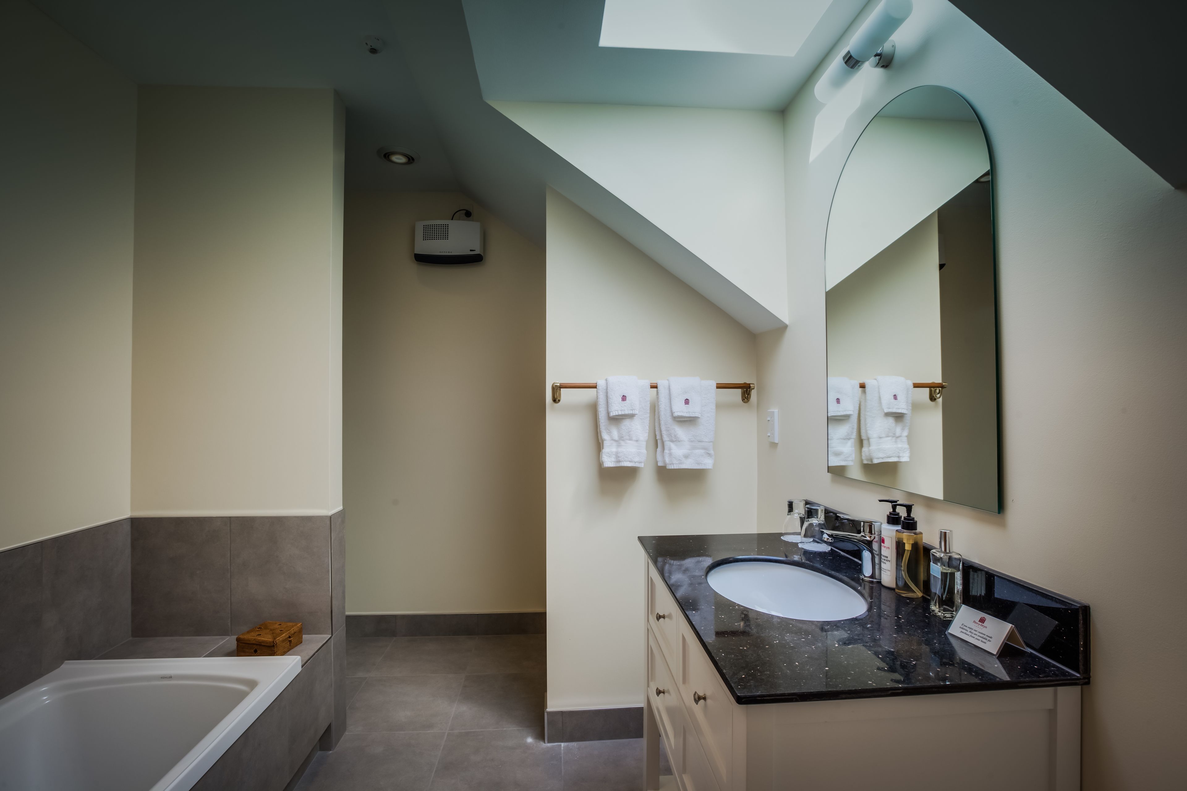 A modern bathroom with a bathtub, a sink with toiletries, and a large mirror.