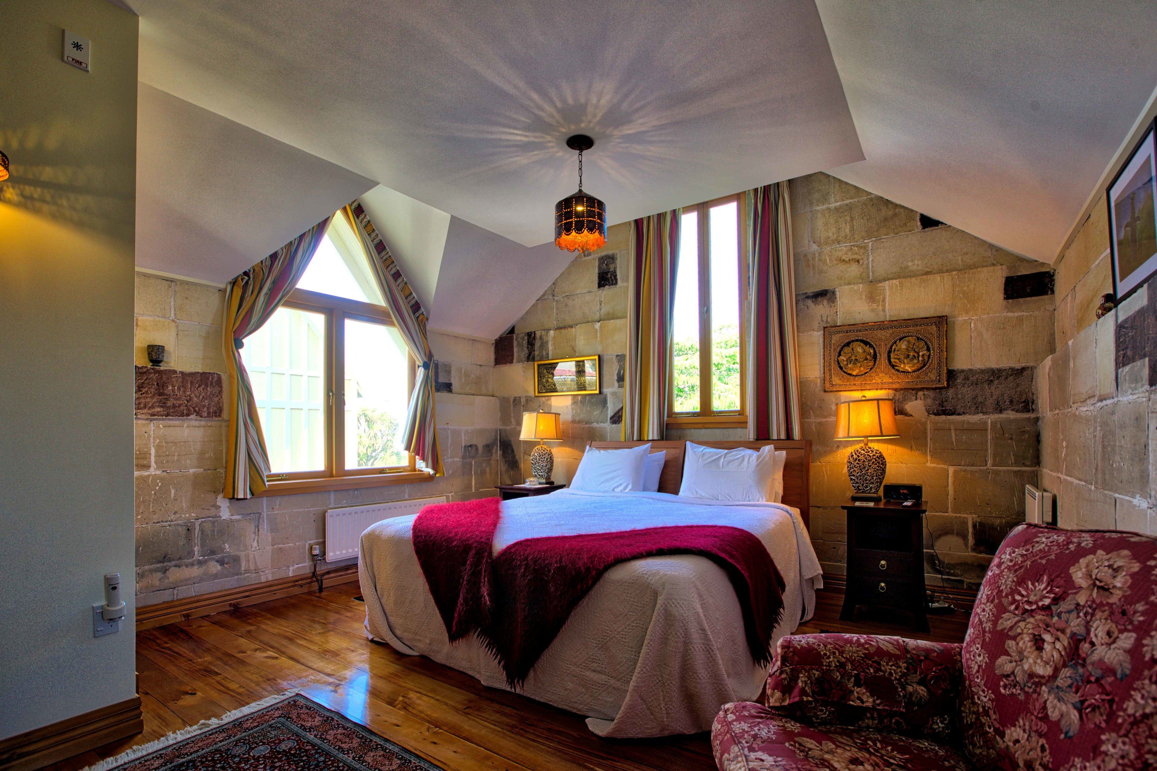 A bedroom with a large bed, a chair, a lamp, and a fireplace.