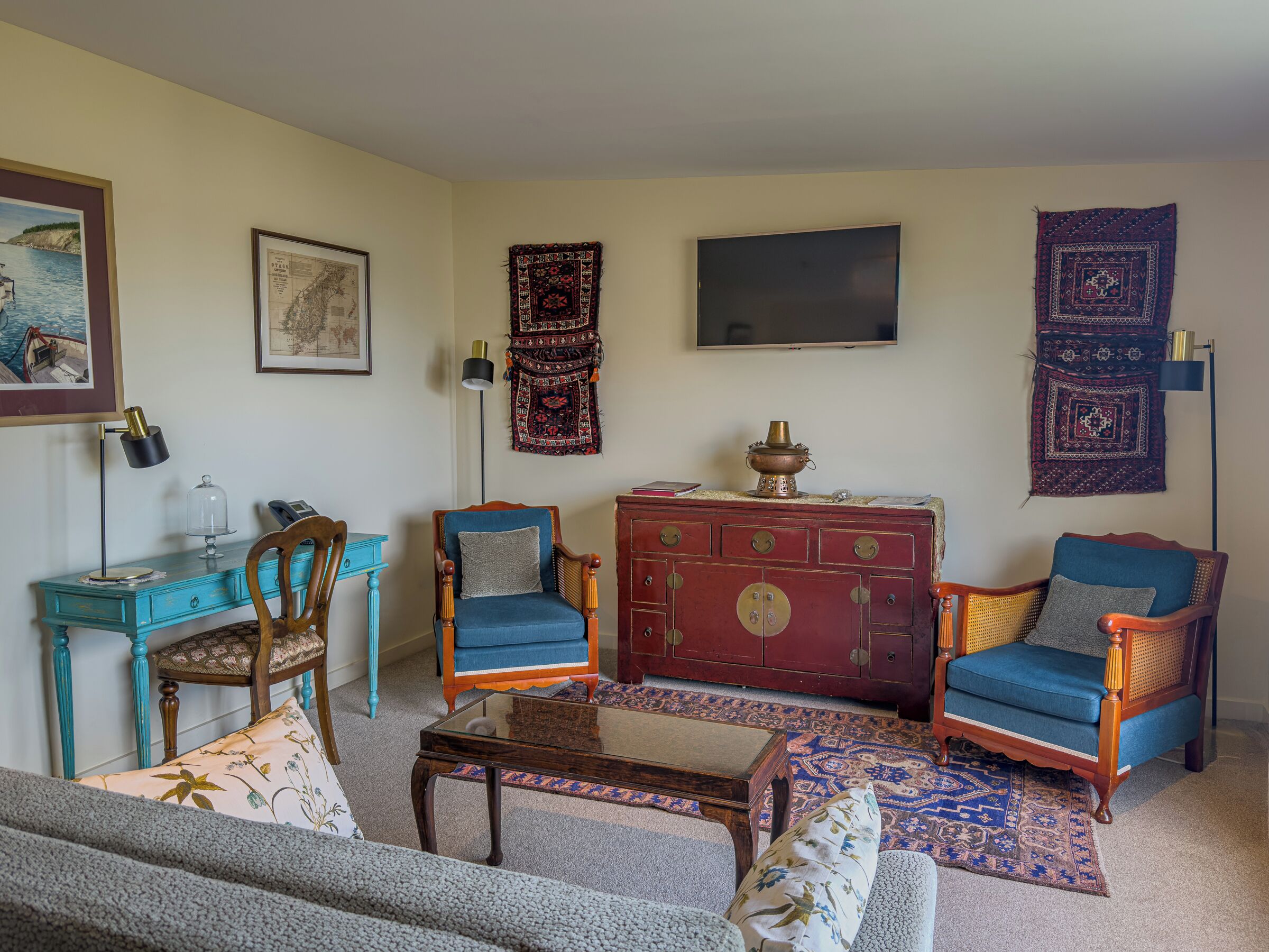 A living room with a sofa, two armchairs, a wooden cabinet, a coffee table, a desk, and a television.