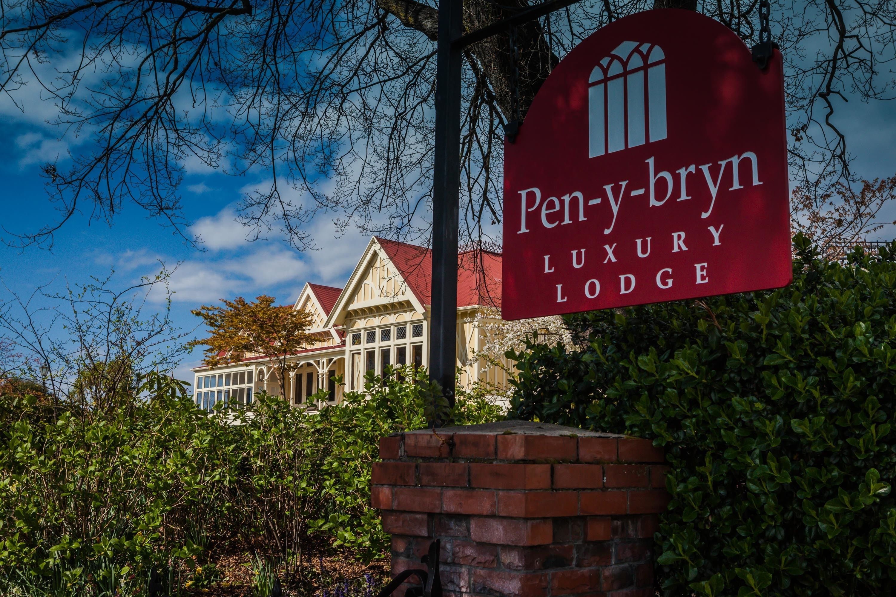 A sign for Pen-y-bryn Luxury Lodge with a traditional building in the background.