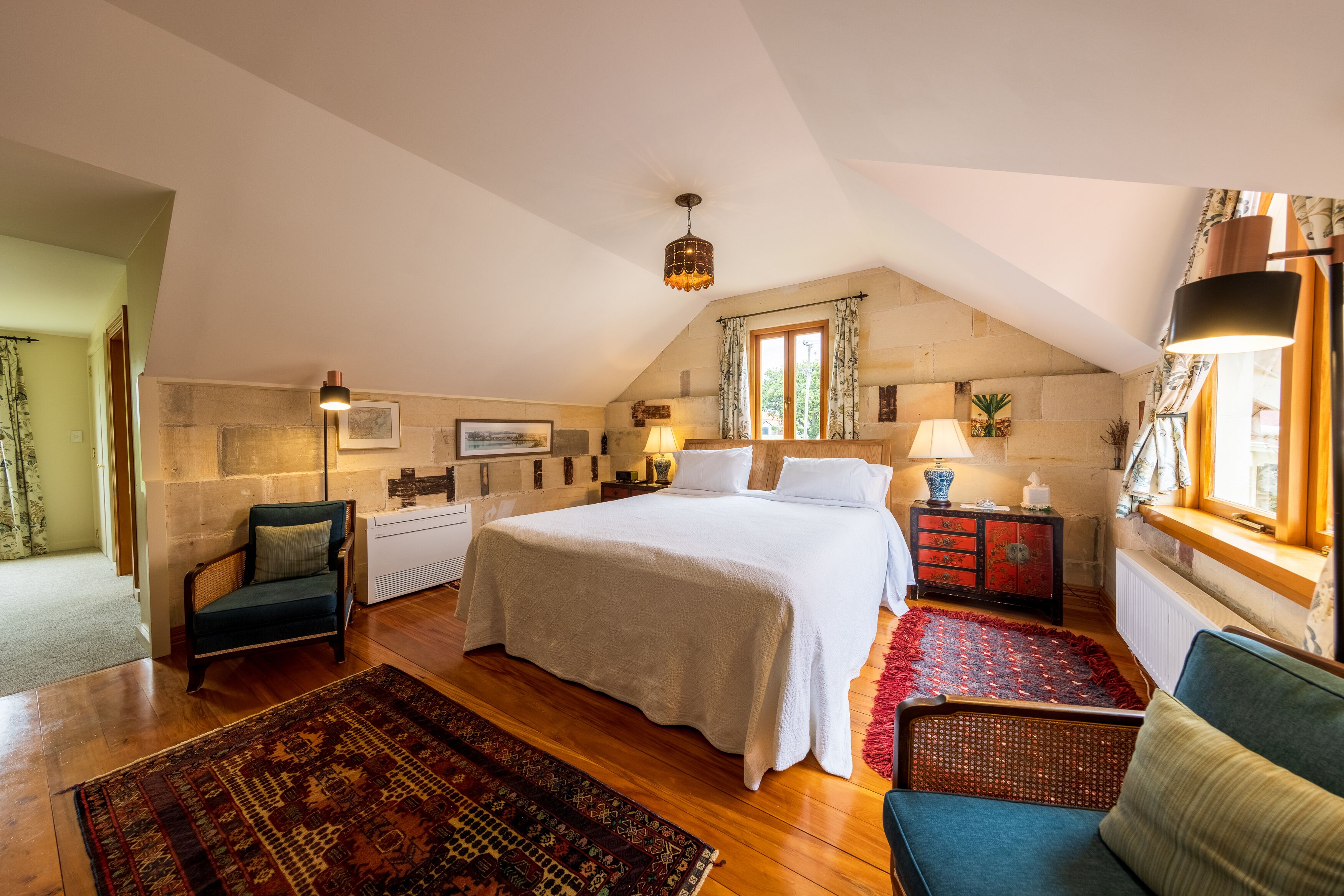 Ein Schlafzimmer mit einem großen Bett, einem Sessel, einem Nachttisch, einer Lampe und einem Fenster mit Vorhängen.
