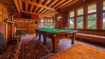 Una habitación de madera con mesa de billar, un banco y ventanas amplias.