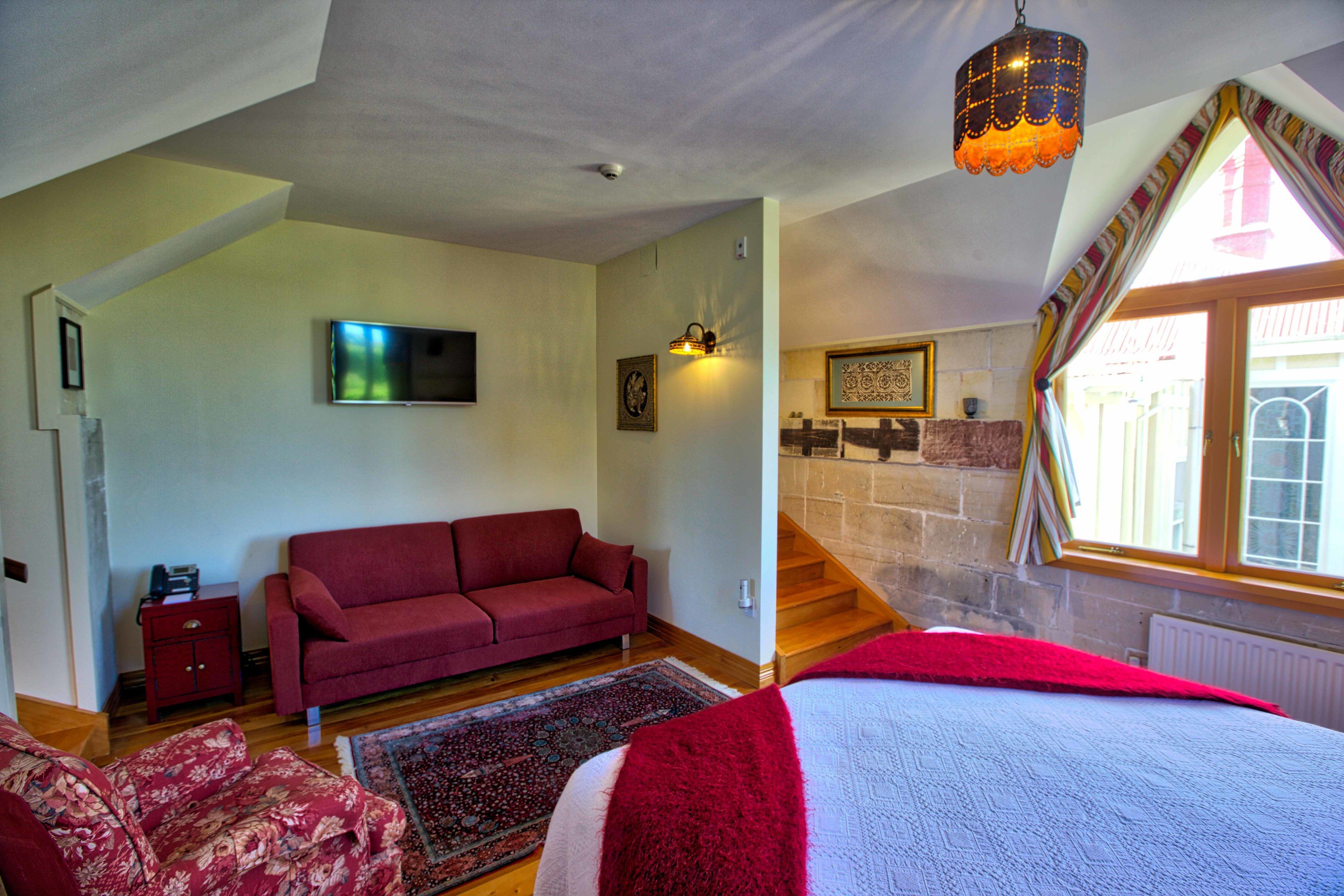 A bedroom with a large bed, a red sofa, a TV, and a staircase leading to an upper level.