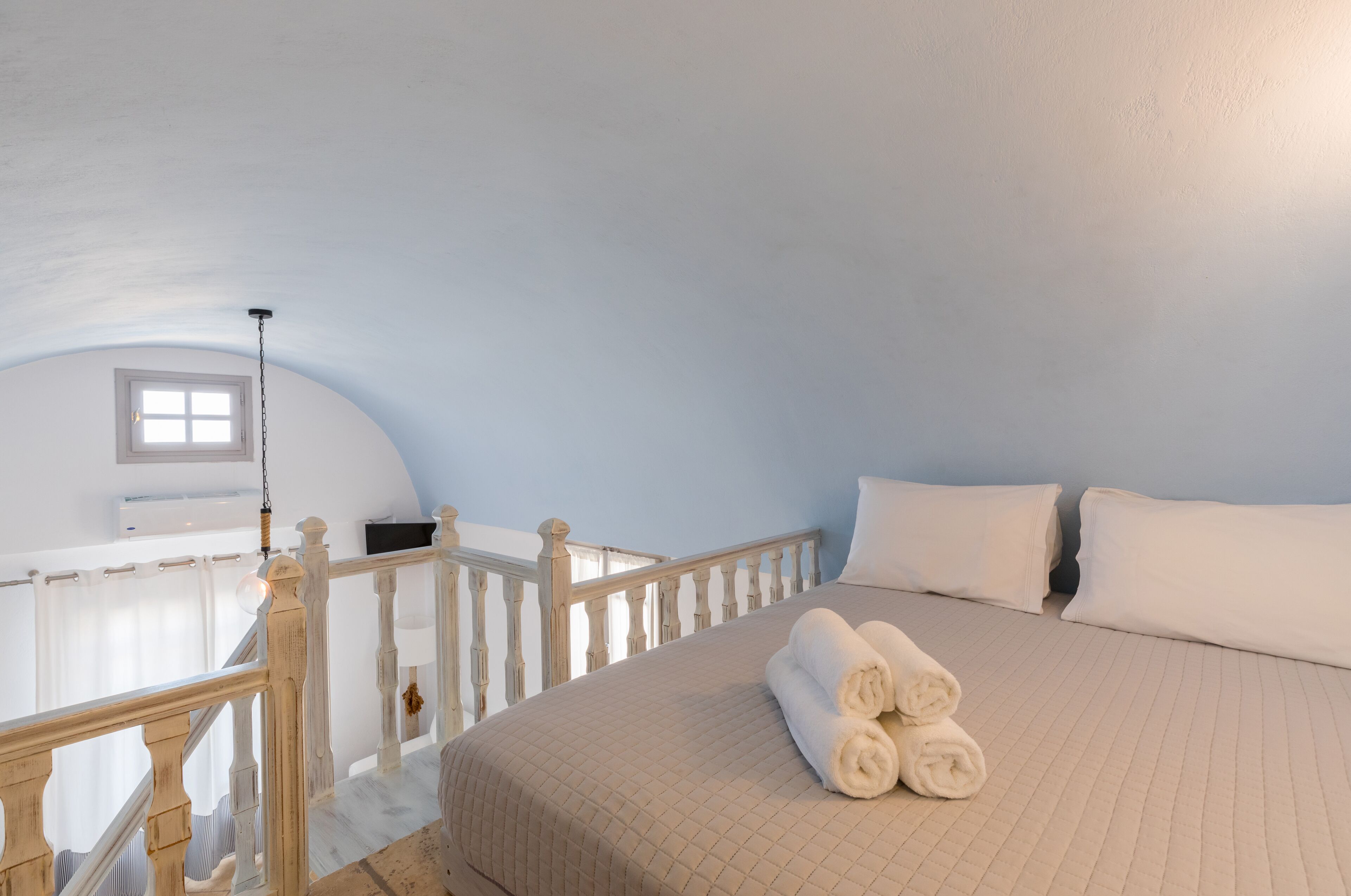 A bedroom with a large bed, white bedding, and a wooden railing.