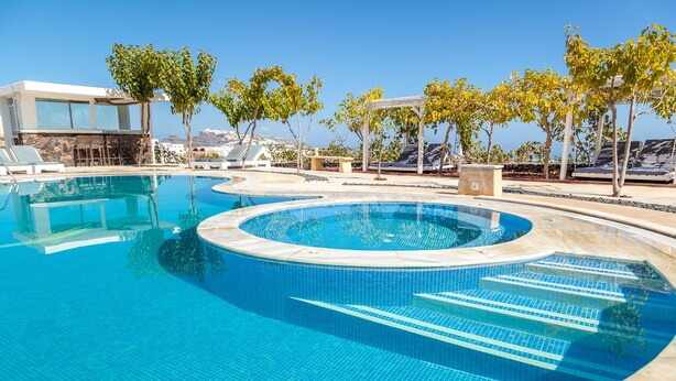 Una piscina de diseño circular, rodeada de sillas de descanso y árboles.