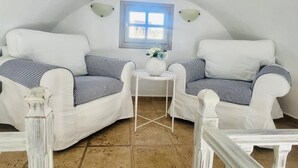 Una habitación acogedora con dos sofás blancos y una mesita, una ventana con vistas y un techo blanco.