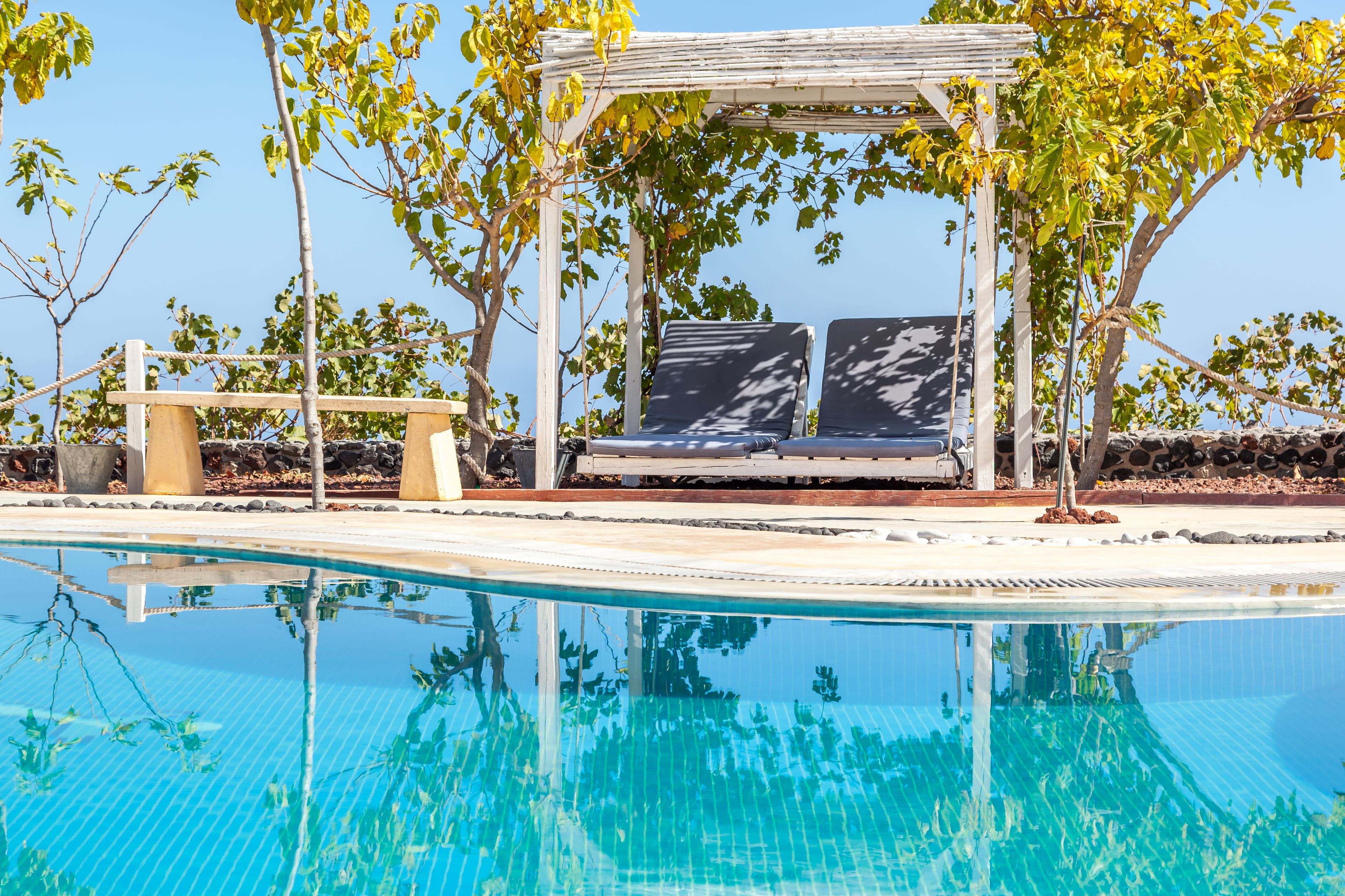 A pool with a pergola and lounge chairs.