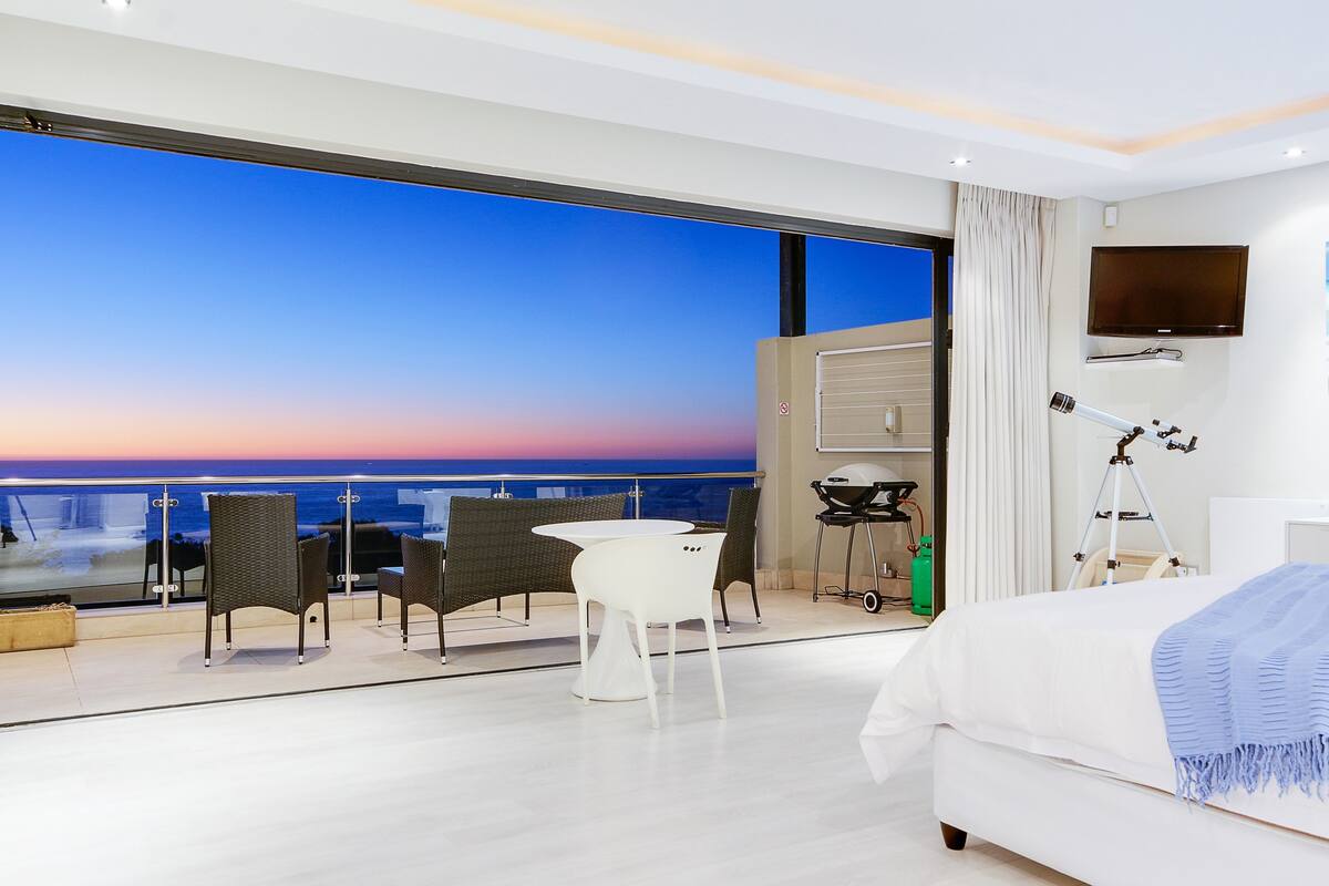 A modern hotel room with a balcony, a bed, a desk, and a TV.