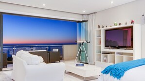 Een moderne hotelkamer met een ruim balkon, een witte bank, een televisie en een boekenkast.