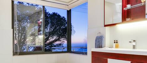 A modern bathroom with a freestanding bathtub, a large window with a view of trees and the sky, and a vanity with a mirror and toiletries.