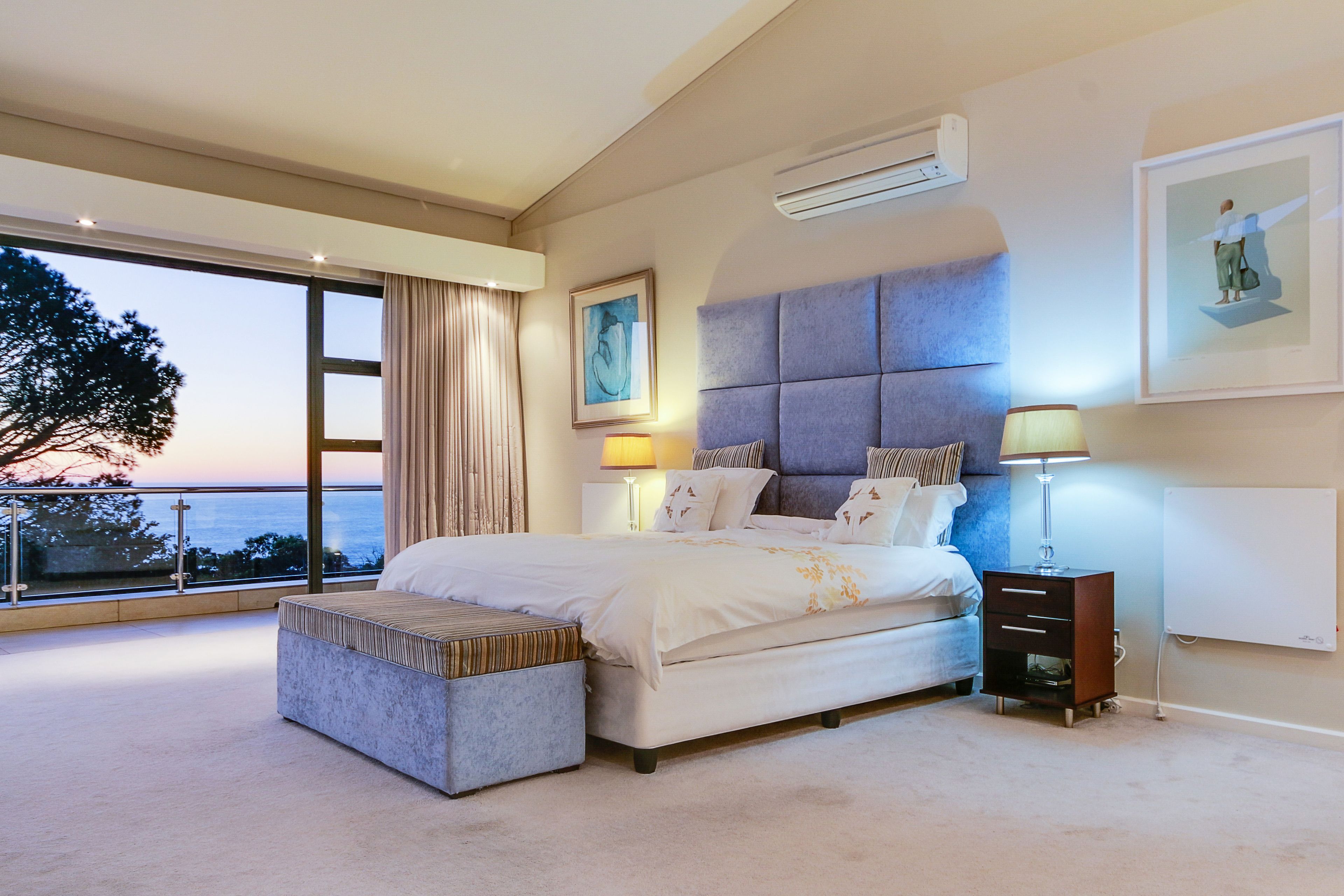 Un dormitorio amplio con una cama grande, una mesita de noche y una mesita auxiliar, con vistas al mar a través de amplias ventanas.