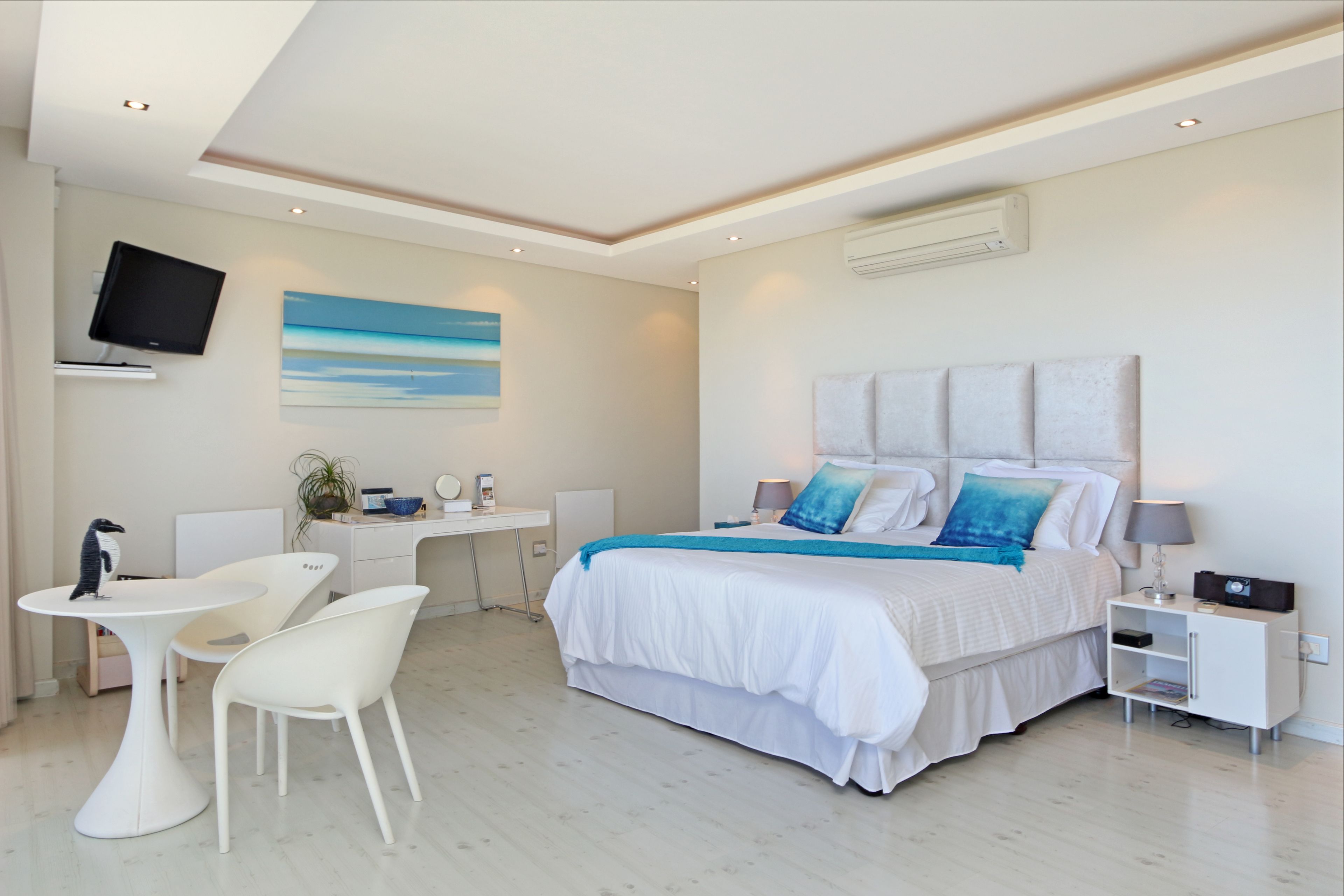 A modern bedroom with a large bed, bedside tables, a desk, and a TV mounted on the wall.