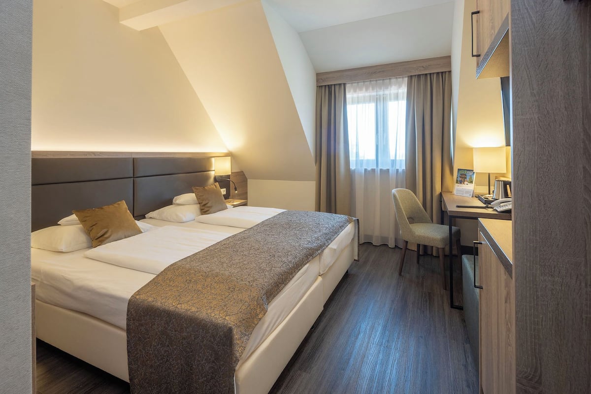A hotel room with a large bed, a desk, a chair, and a window with curtains.