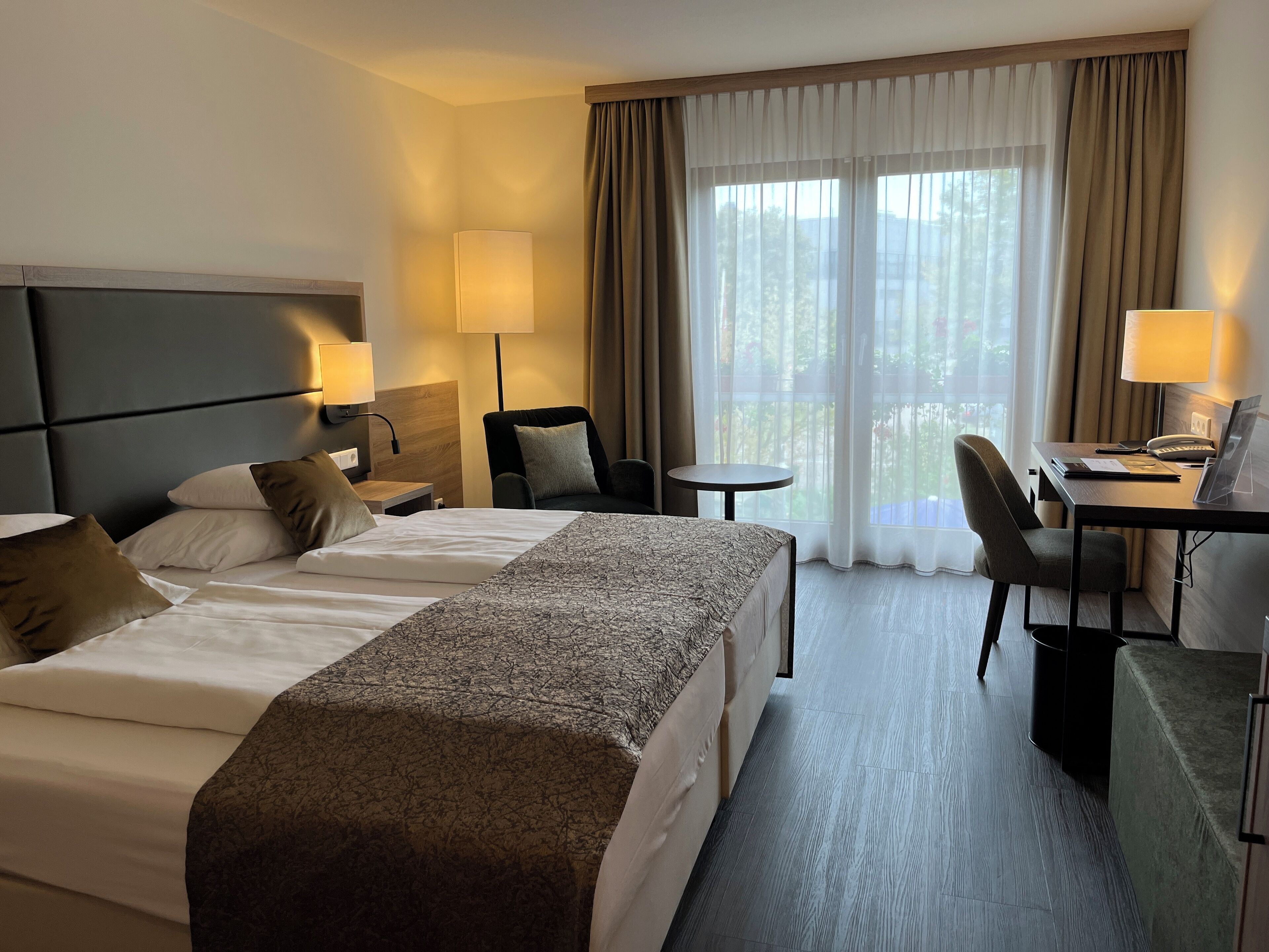 Een hotelkamer met twee bedden, een bureau, een stoel en uitzicht op de omgeving.