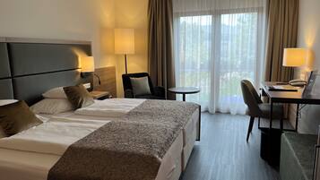 Een hotelkamer met twee bedden, een bureau, een stoel en uitzicht op de omgeving.