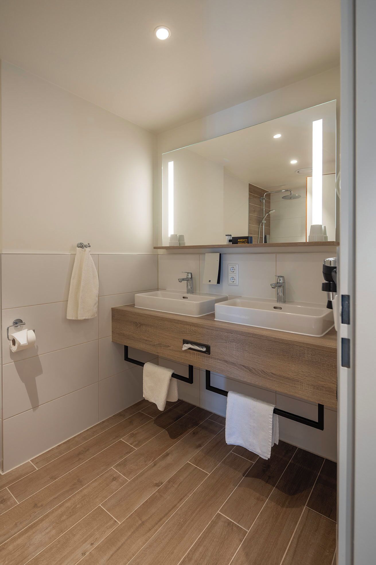 A modern bathroom with two sinks, a large mirror, and a shower.