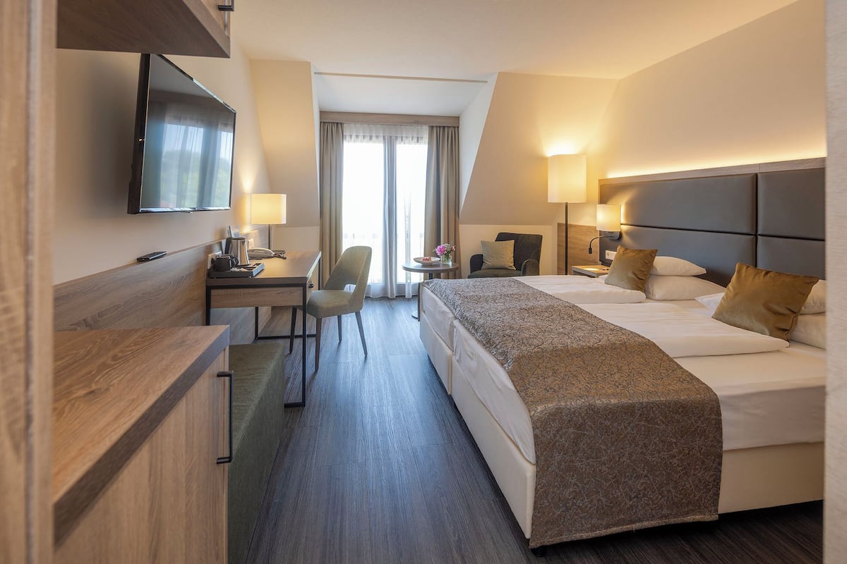 A hotel room with a bed, desk, chair, and a TV mounted on the wall.