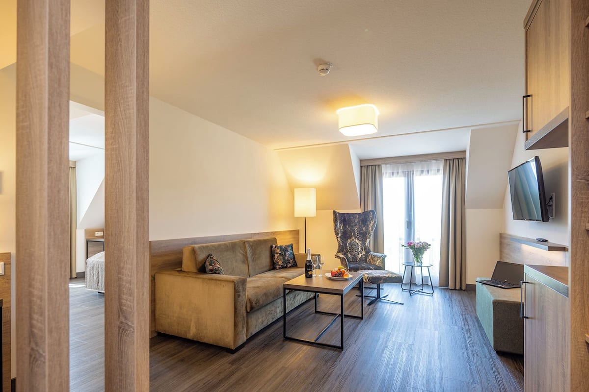 A modern hotel room with a sofa, a coffee table, a TV, and a dining table with a laptop.