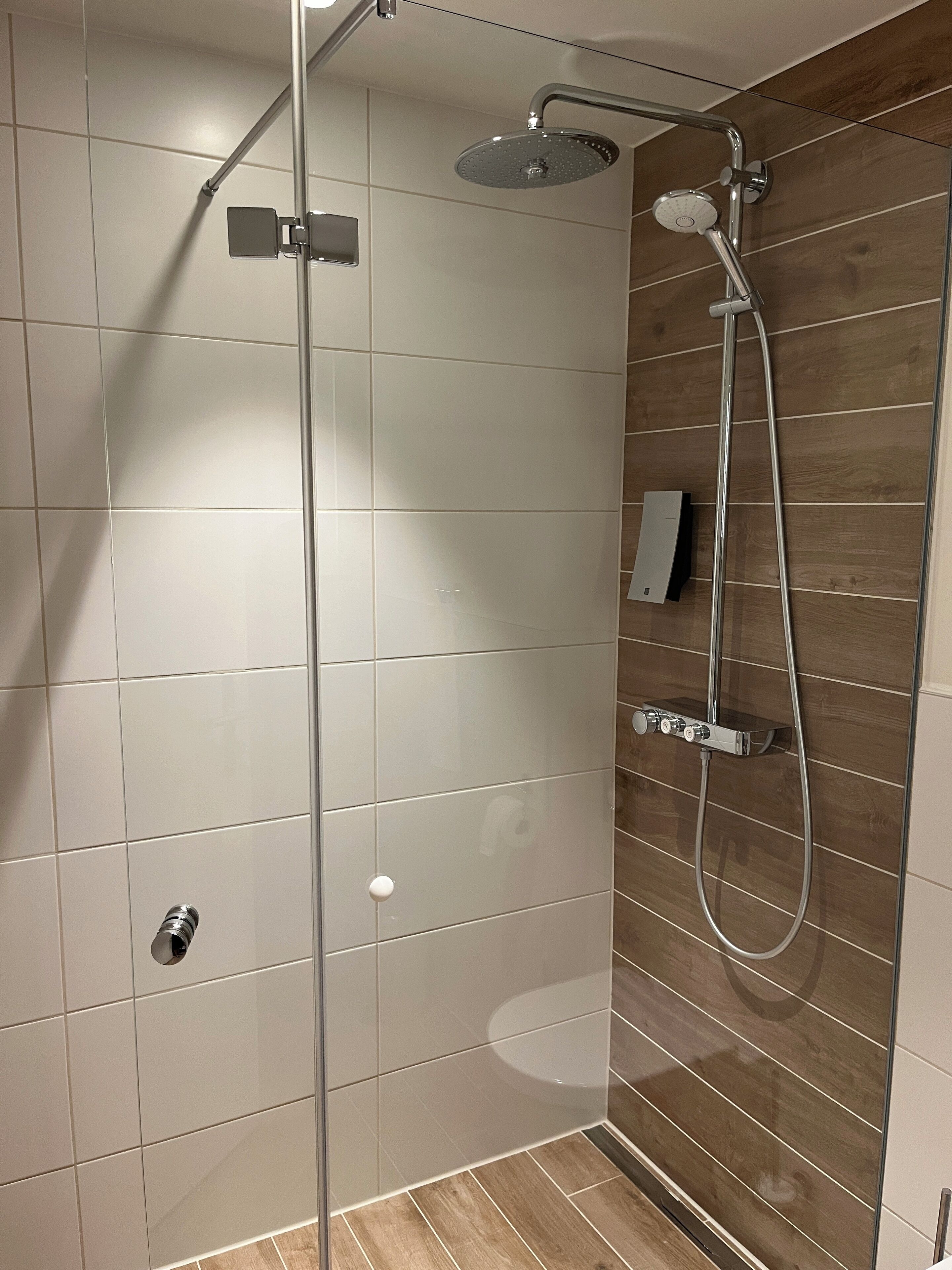 A modern shower with a glass door, a handheld showerhead, and a wall-mounted control panel.