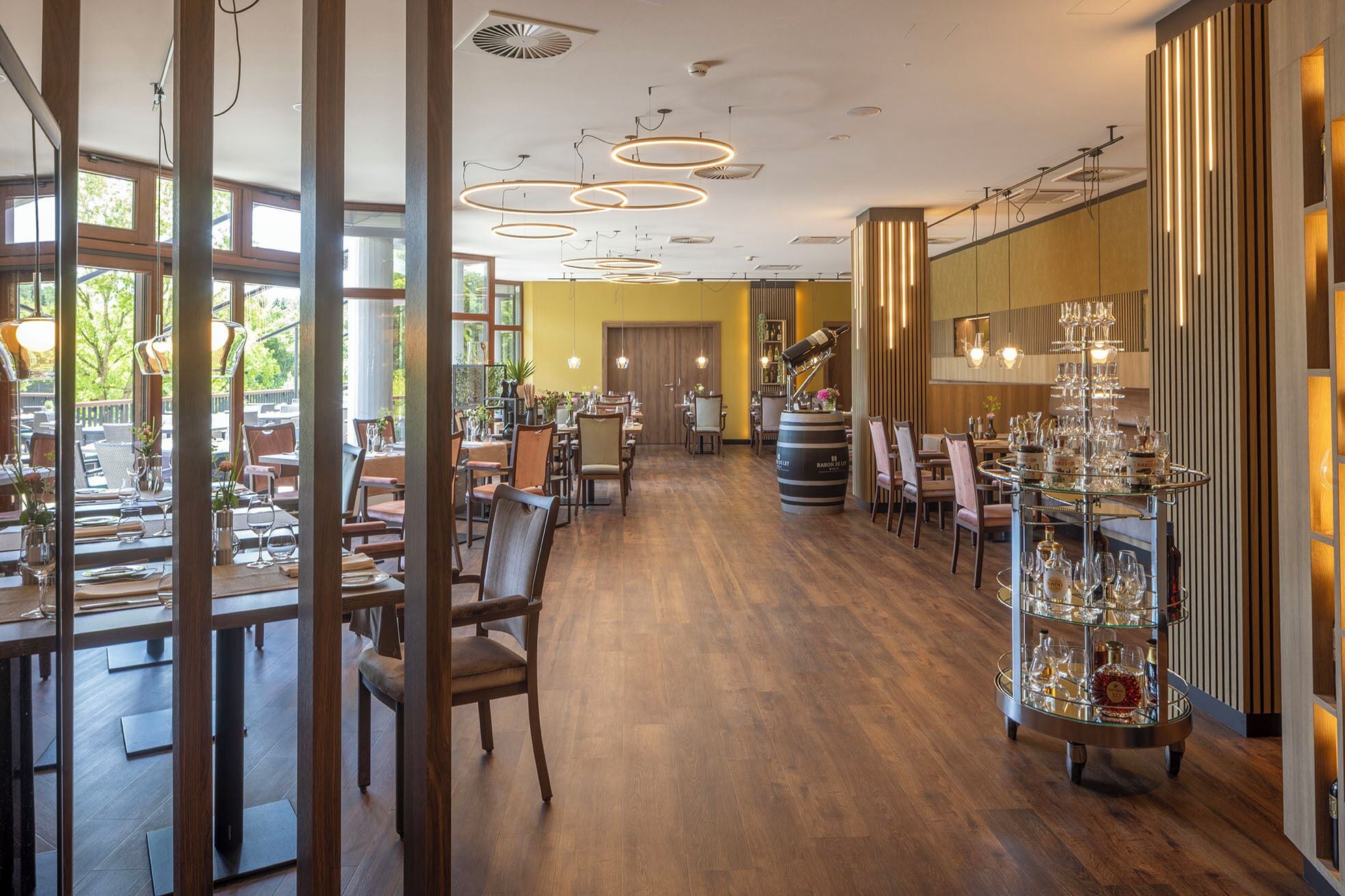 Ein Restaurant mit Holzböden, mehreren Essplätzen und einer Bar mit Weinauslage.